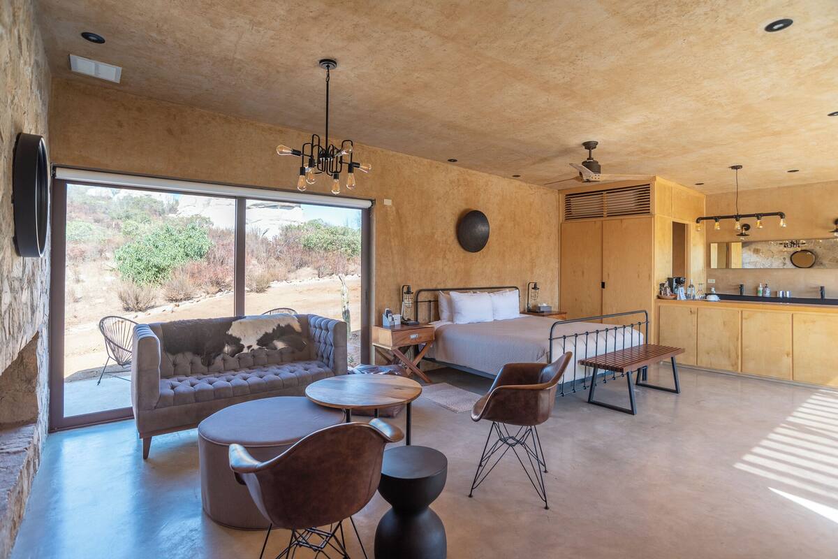 Una habitación amplia con una cama grande, un sofá, una mesa de comedor y sillas. Cuenta con una zona de cocina con un fregadero y armarios.