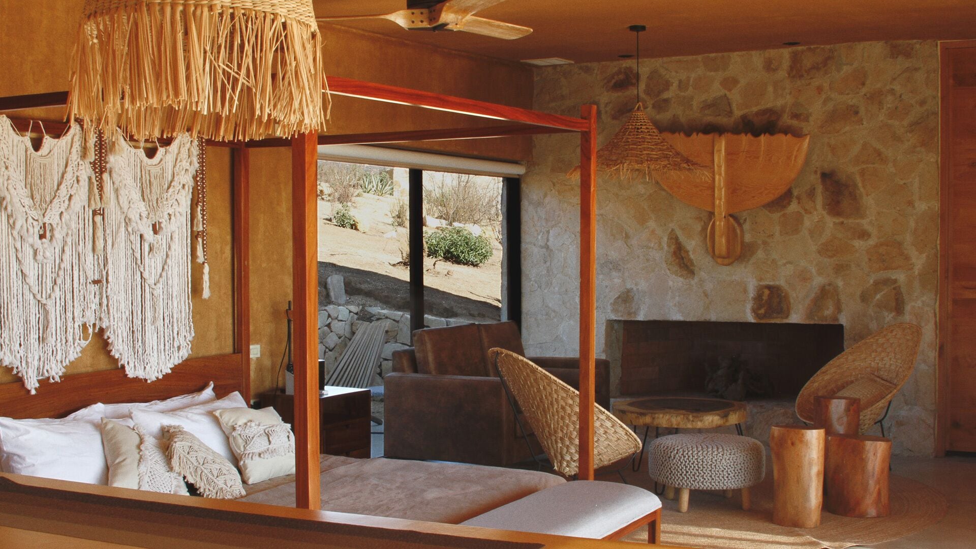 A room with a bed, a stone wall, a fireplace, and a view of the outdoors.