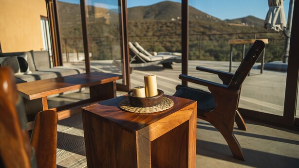 Une pièce baignée de lumière, meublée de meubles en bois, avec une table décorée de bougies et une vue sur les montagnes par de grandes fenêtres.