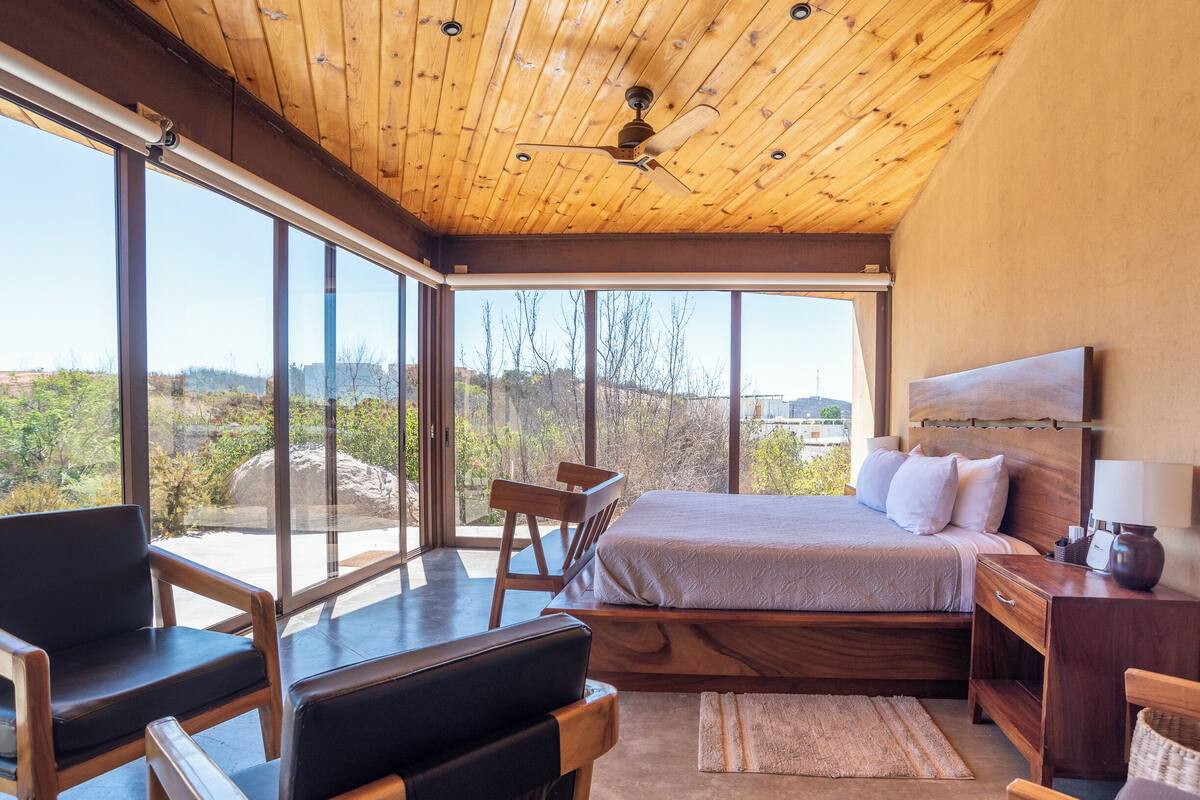 Un dormitorio con una cama grande, techo de madera y vistas al exterior.