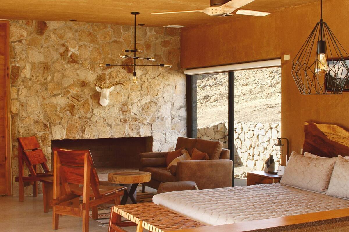 Un dormitorio con pared de piedra, cama, ventilador de techo de madera y cabeza de venado montada.