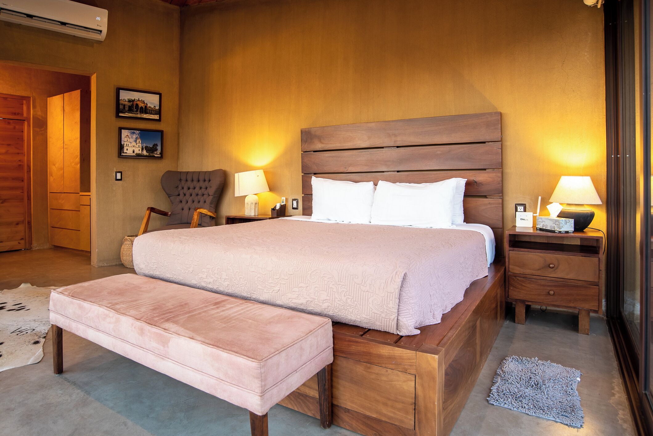 Une chambre à coucher avec un grand lit, une tête de lit en bois, deux tables de chevet avec des lampes, un banc et un tapis.