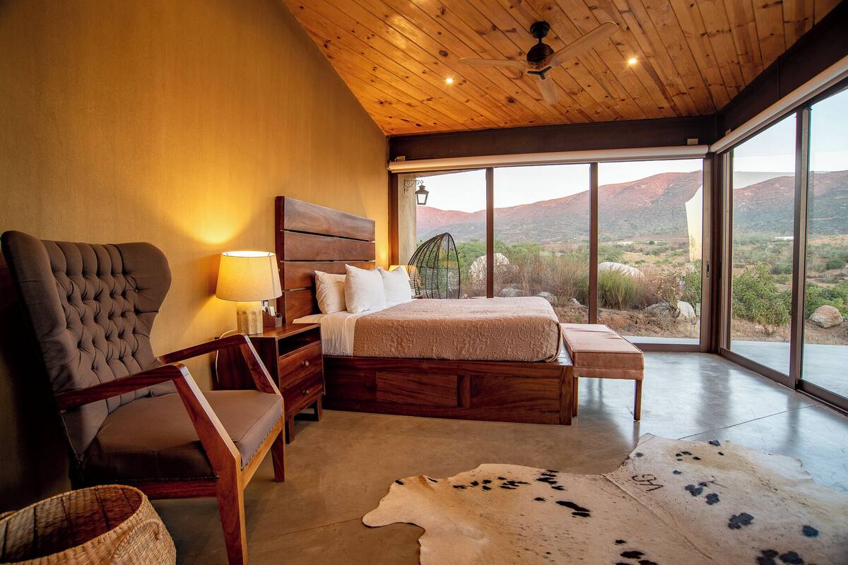 Un dormitorio con una cama grande, muebles de madera, vistas al paisaje desértico y un ventilador de techo.