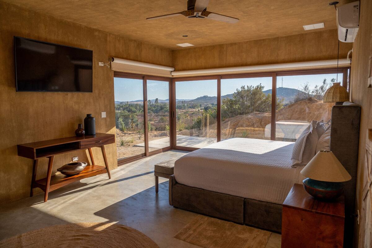Un dormitorio con una cama grande, un escritorio, un televisor y vistas al exterior.