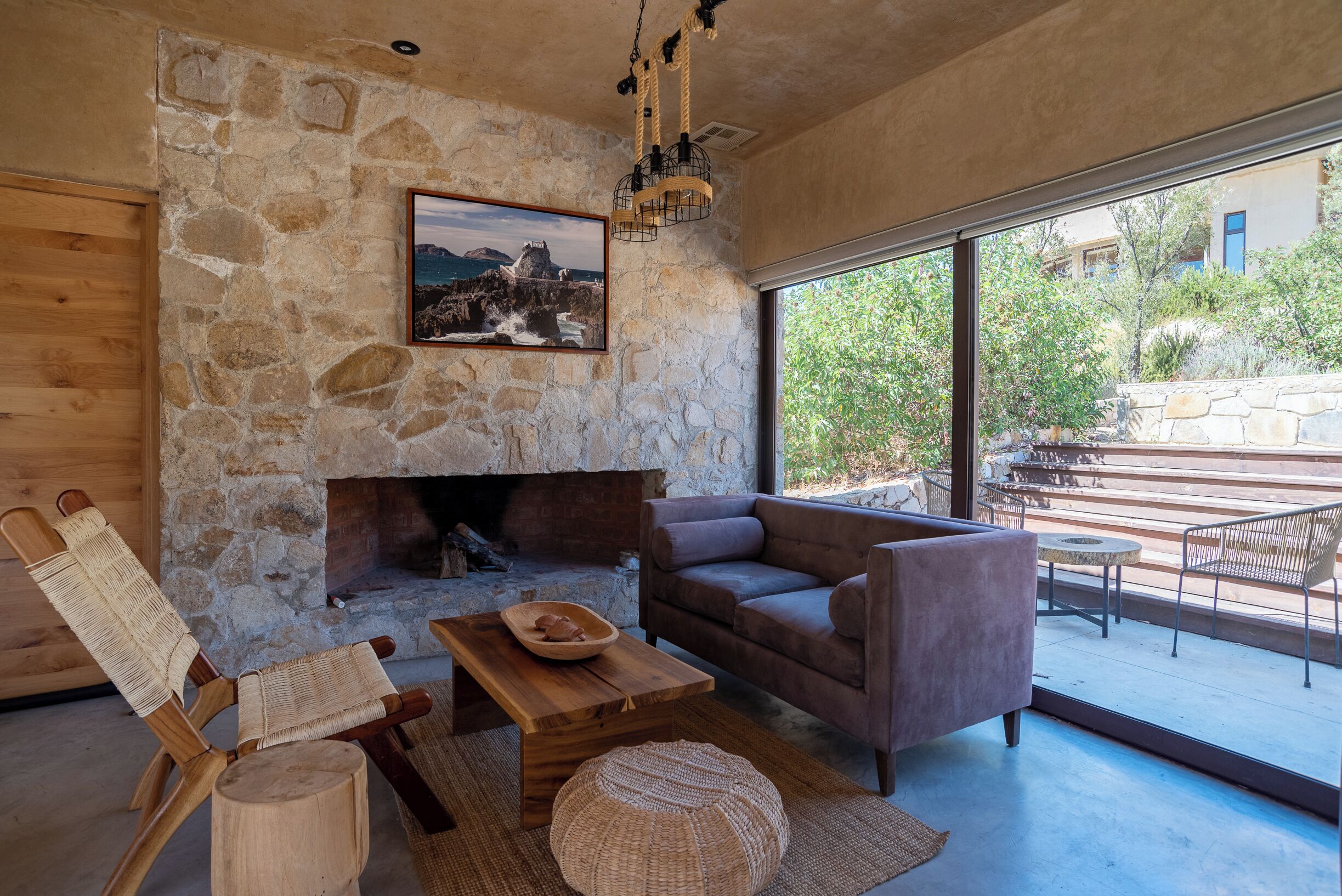 Una sala de estar acogedora con una pared de piedra, una chimenea, un sofá cómodo y un gran ventanal con vistas al exterior.