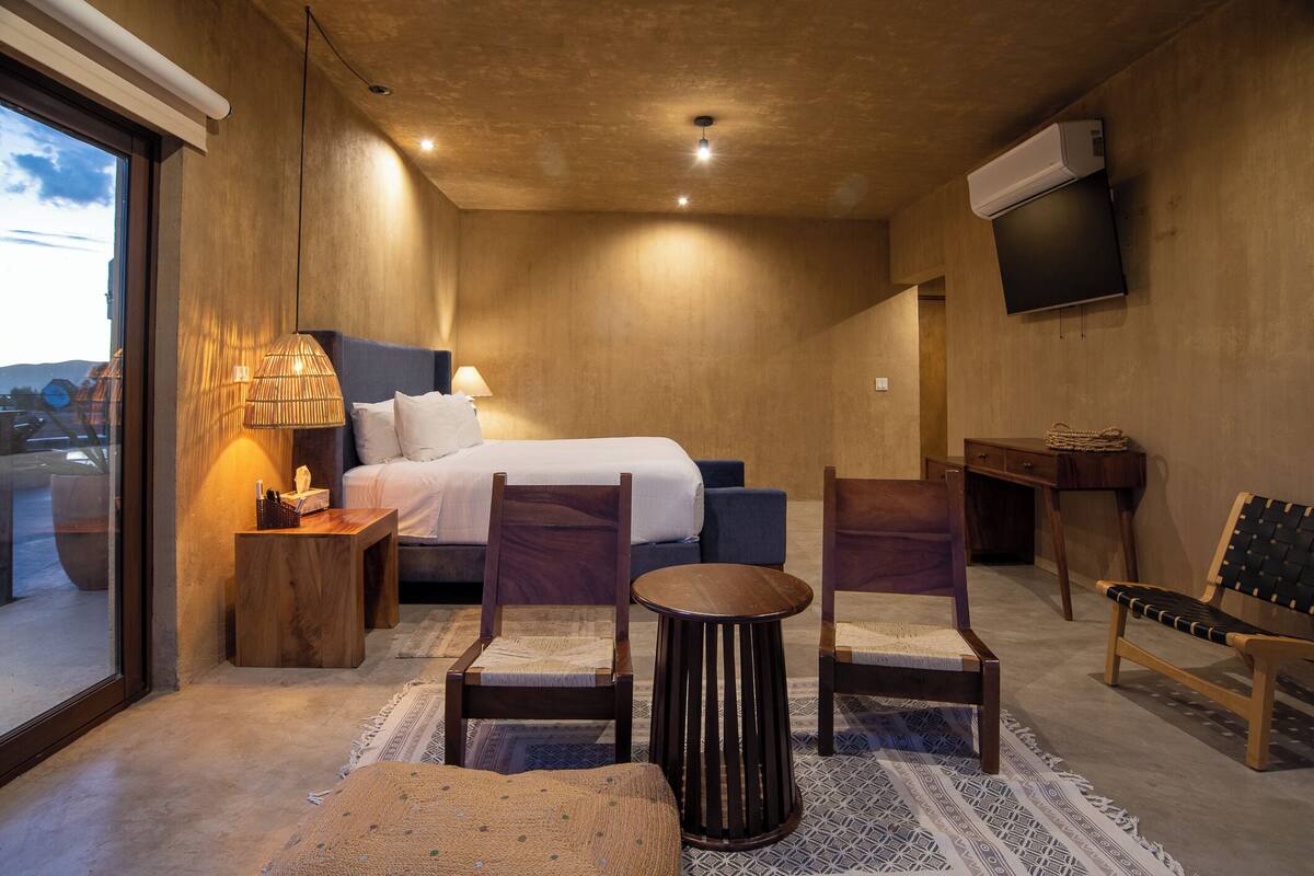 Una habitación de hotel moderna con una cama grande, muebles de madera, una pequeña mesa redonda y un televisor montado en la pared.