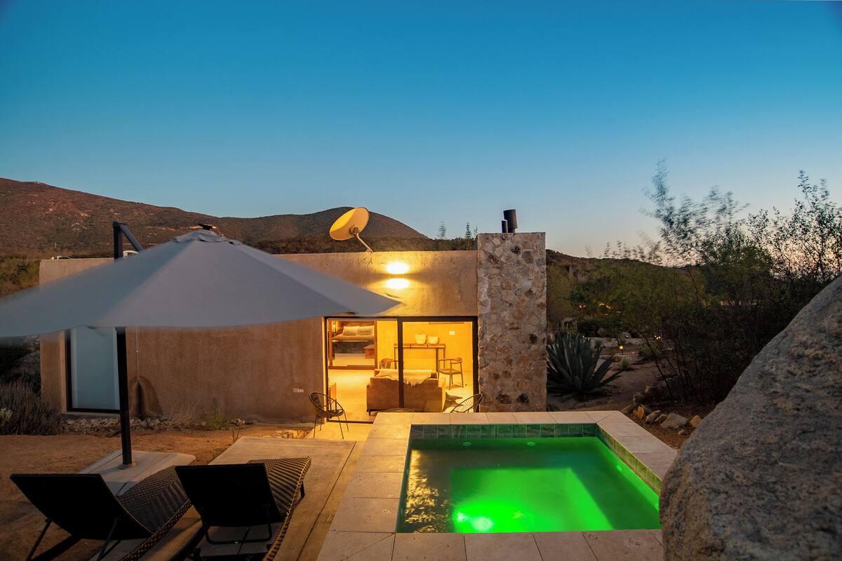 Zona de piscina exterior moderna con muro de piedra, sillones de descanso y una antena parabólica.