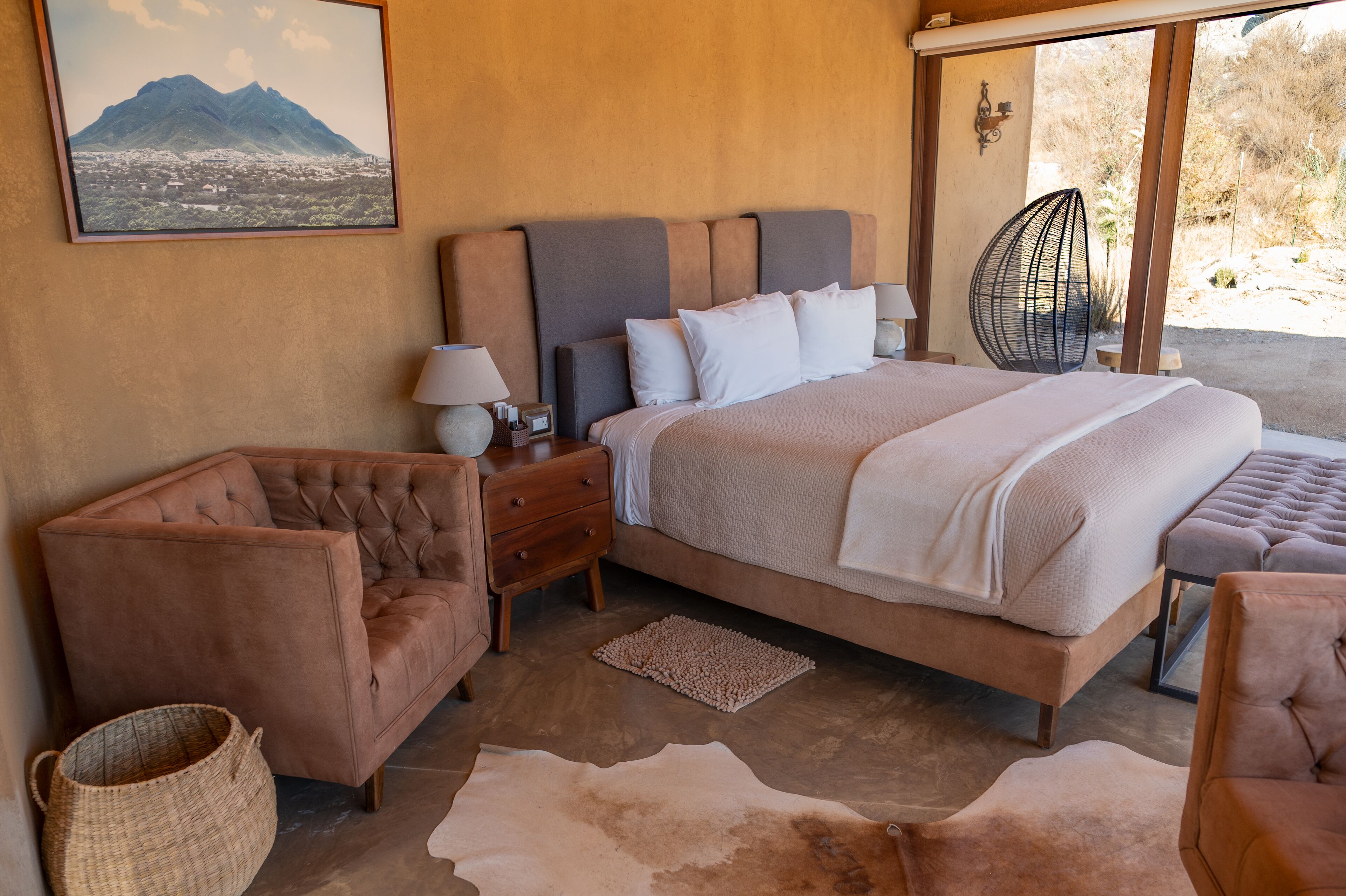 A bedroom with a large bed, a nightstand, a lamp, a chair, and a view of the outdoors.