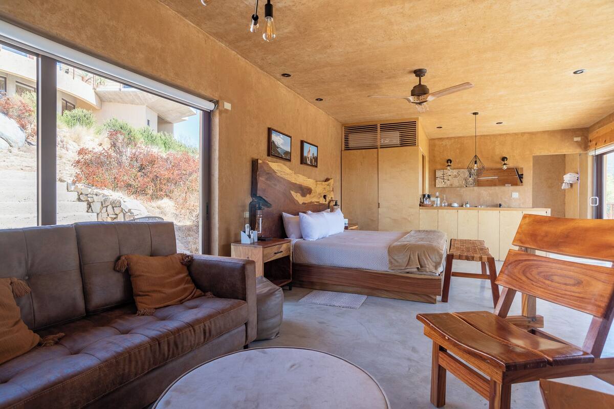 Un dormitorio moderno con una cama grande, un banco de madera, un sofá y un escritorio.