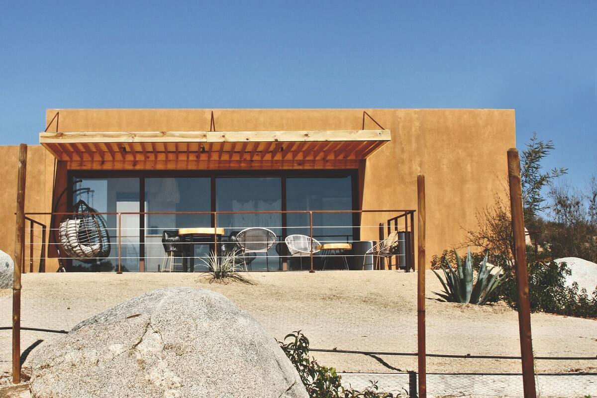 Un edificio moderno con un amplio ventanal, mesas al aire libre y una pérgola de madera.