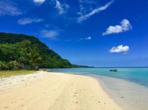 Une plage à l’eau turquoise et limpide, un rivage sablonneux et, en arrière-plan, une colline verdoyante.