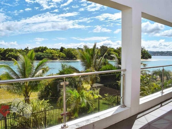 A balcony with a view of a tropical landscape, including a body of water and lush greenery.