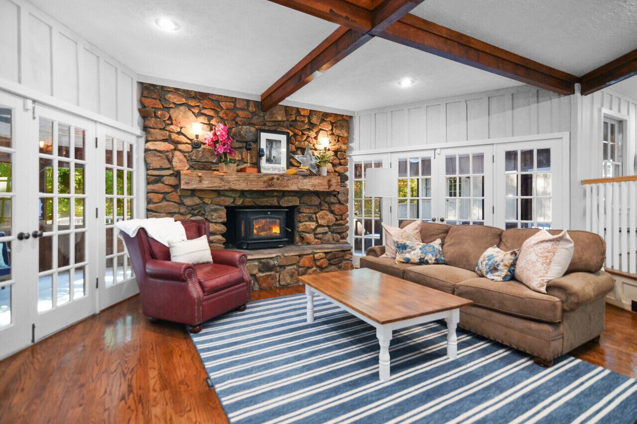 A cozy living room with a stone fireplace, a red leather armchair, a brown sofa, and a striped rug.