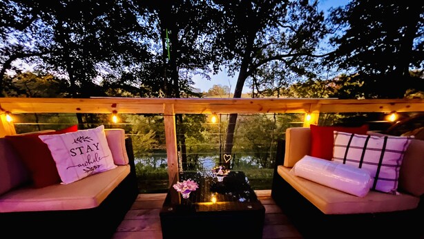 Eine gemütliche Sitzgruppe im Freien mit zwei gepolsterten Sofas und einem Couchtisch in der Mitte, umgeben von Lichterketten und Blick auf Bäume.