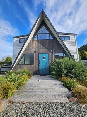 A modern house with a triangular roof, a blue door, and a gravel pathway leading to it.