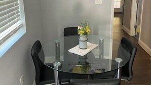 Un coin repas avec une table en verre entourée de chaises noires, un vase avec des fleurs jaunes et trois tableaux encadrés accrochés au mur.