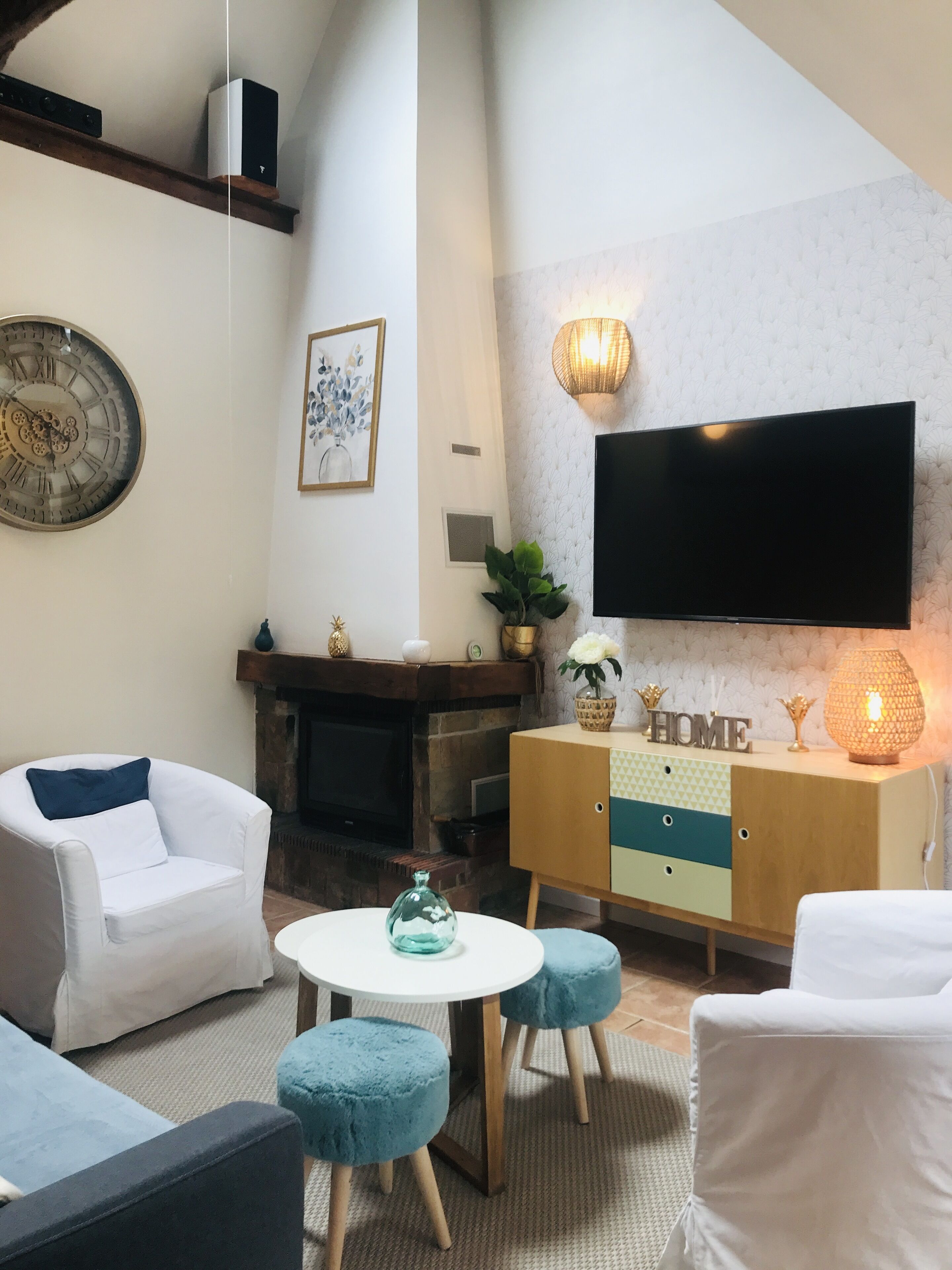 A modern living room with a fireplace, a mounted TV, and a cozy seating area with ottomans and a sofa.