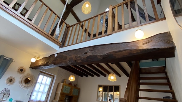 Une pièce de style loft avec un plafond haut, des poutres apparentes, un escalier, un canapé bleu et un coin repas.