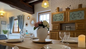 Un coin repas avec une table en bois dressée pour quatre personnes, un vase rempli de fleurs et une bougie posée sur la table.