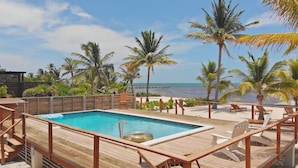 A wooden deck with a swimming pool, lounge chairs, and palm trees. - Ocean Front  Home with pier. (San Pedro Ambergris Caye)