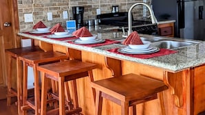 A kitchen with wooden bar stools, granite countertops, and a stainless steel refrigerator. - Ocean Front  Home with pier. (San Pedro Ambergris Caye)