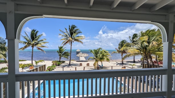 A view from a covered balcony overlooking a beach with palm trees and a pool. - Ocean Front  Home with pier. (San Pedro Ambergris Caye)