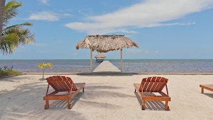 A beachside lounge with two wooden chairs and a thatched-roof structure. - Ocean Front  Home with pier. (San Pedro Ambergris Caye)