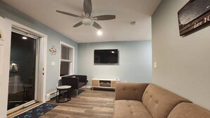 A living room with a ceiling fan, a flat-screen TV, a sofa, and a small table. - Minutes to Walnut Beach, newly renovated 3 bedroom home (Milford)