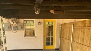 Un espacio exterior techado con piso de concreto, una puerta amarilla y una valla de madera.
