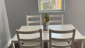 Un comedor con una mesa y cuatro sillas, una ventana con persianas y una planta en maceta sobre la mesa.