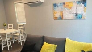 Una sala moderna con un sofá seccional gris, una mesa de comedor con sillas y un equipo de aire acondicionado.