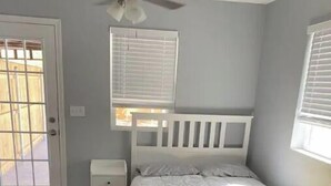 Un dormitorio con una cama, una mesita de noche, una ventana con persianas y una puerta.