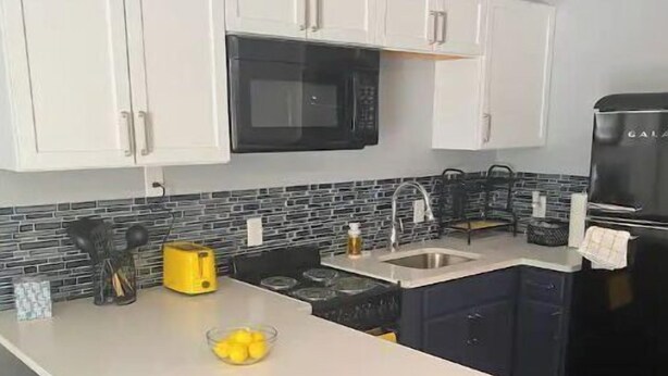 Una cocina compacta con armarios blancos, un microondas negro, un refrigerador negro y una pequeña isla con un fregadero.