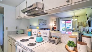 Een moderne keuken met een witte kookplaat, een blauwe waterkoker en een keukeneiland met potten en een plant.