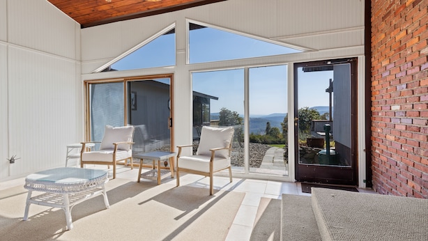 A sunlit patio with a wooden ceiling, large glass doors, and a view of the landscape.