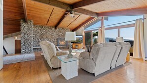 A cozy living room with a stone fireplace, comfortable seating, and a large window offering a view.