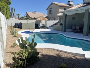 A swimming pool with a curved edge, surrounded by a patio area with chairs and a table.