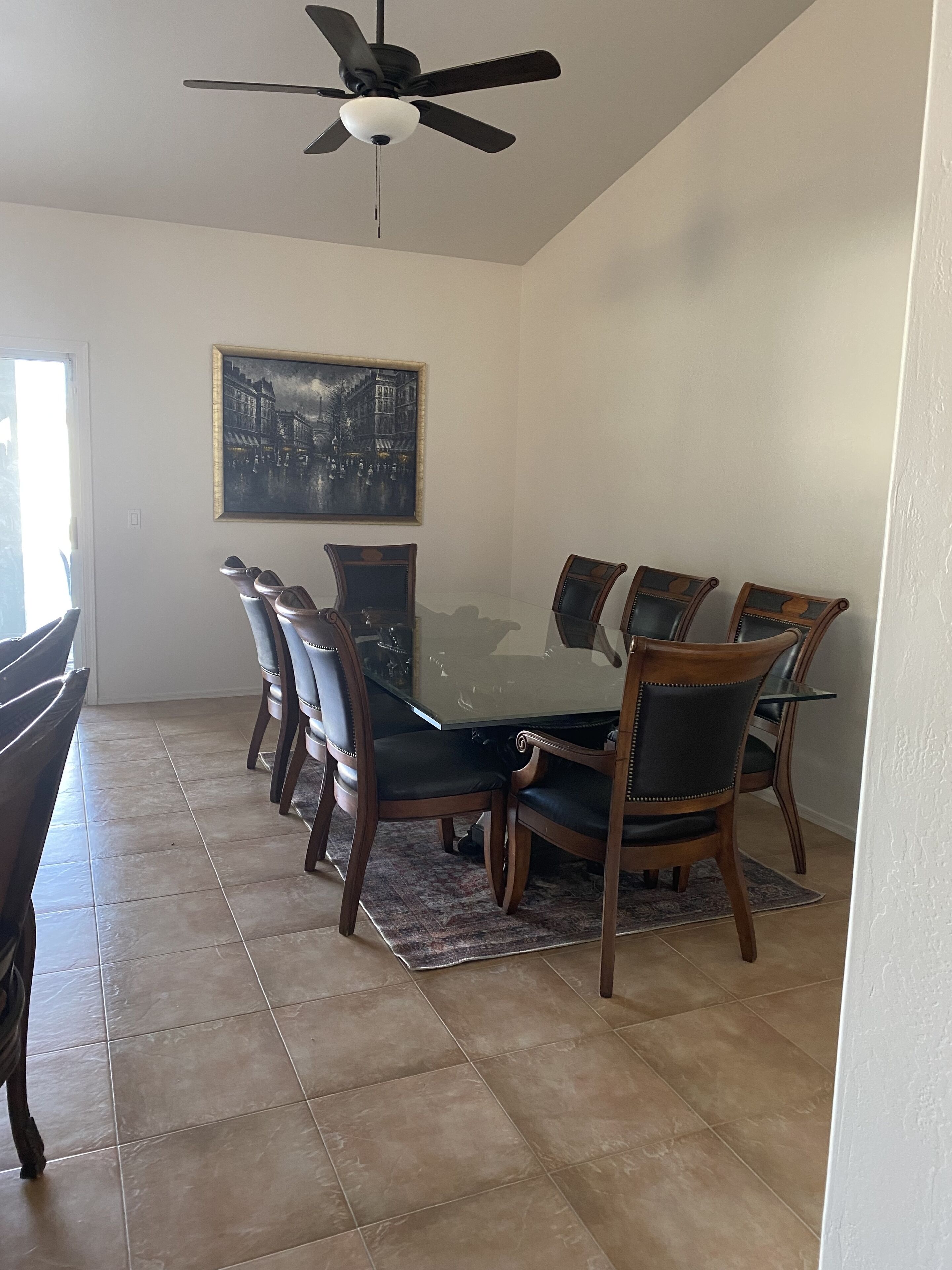 Una sala da pranzo con un tavolo in vetro circondato da sei sedie, una ventola a soffitto e un quadro appeso al muro.