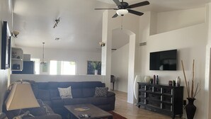 A living room with a sofa, coffee table, and TV. There is a ceiling fan, a lamp, and a plant. - Free Heated Pool! No pet fee!!  Electric vehicle charger in garage.  (Phoenix)
