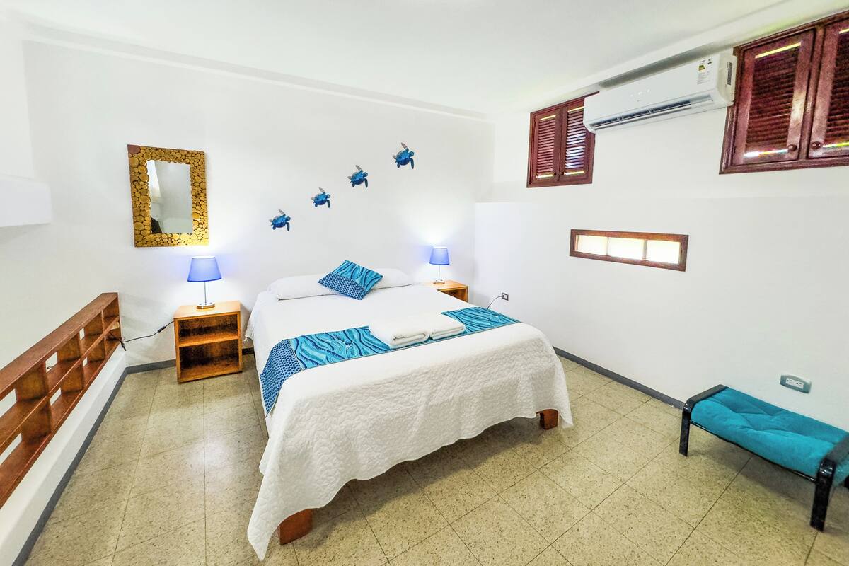 Ein Schlafzimmer mit Bett, Nachttischen, einem Spiegel, Wanddekorationen und einem Fenster mit Fensterläden.