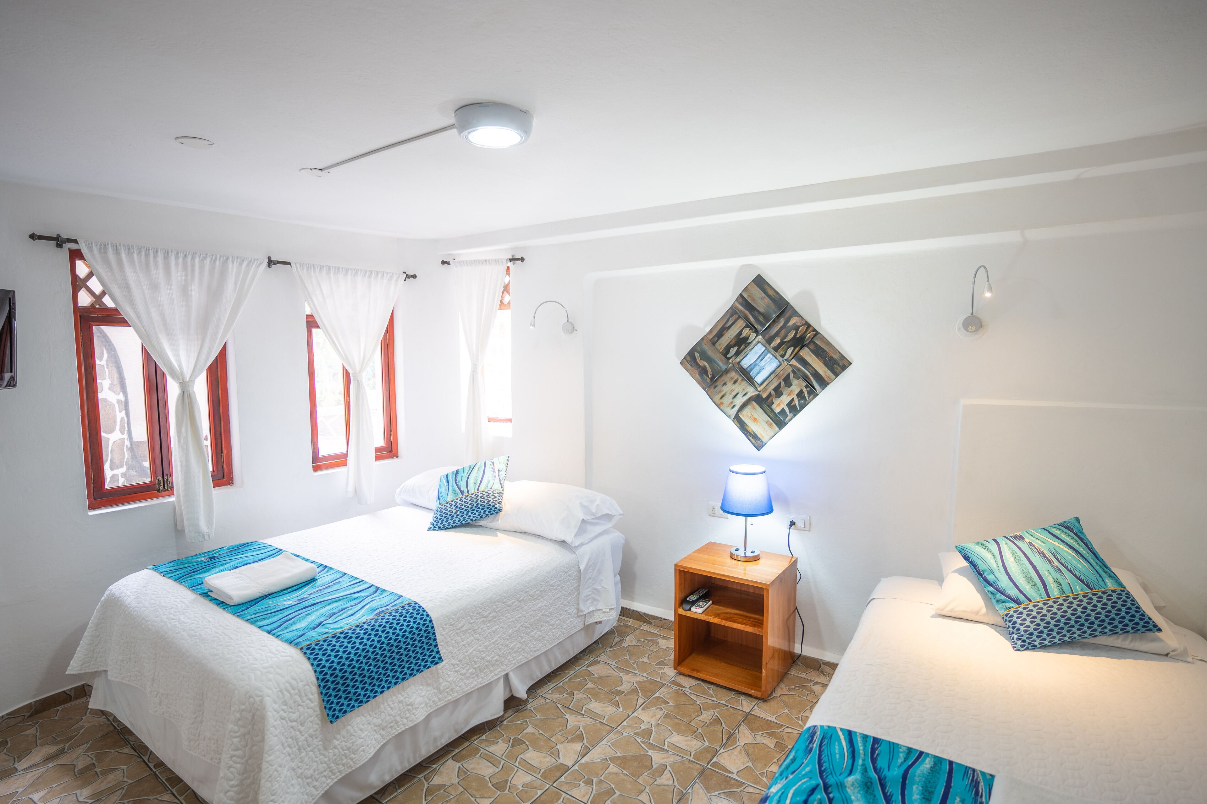 Una habitación con dos camas, una mesita de noche con lámpara y una obra de arte en la pared.