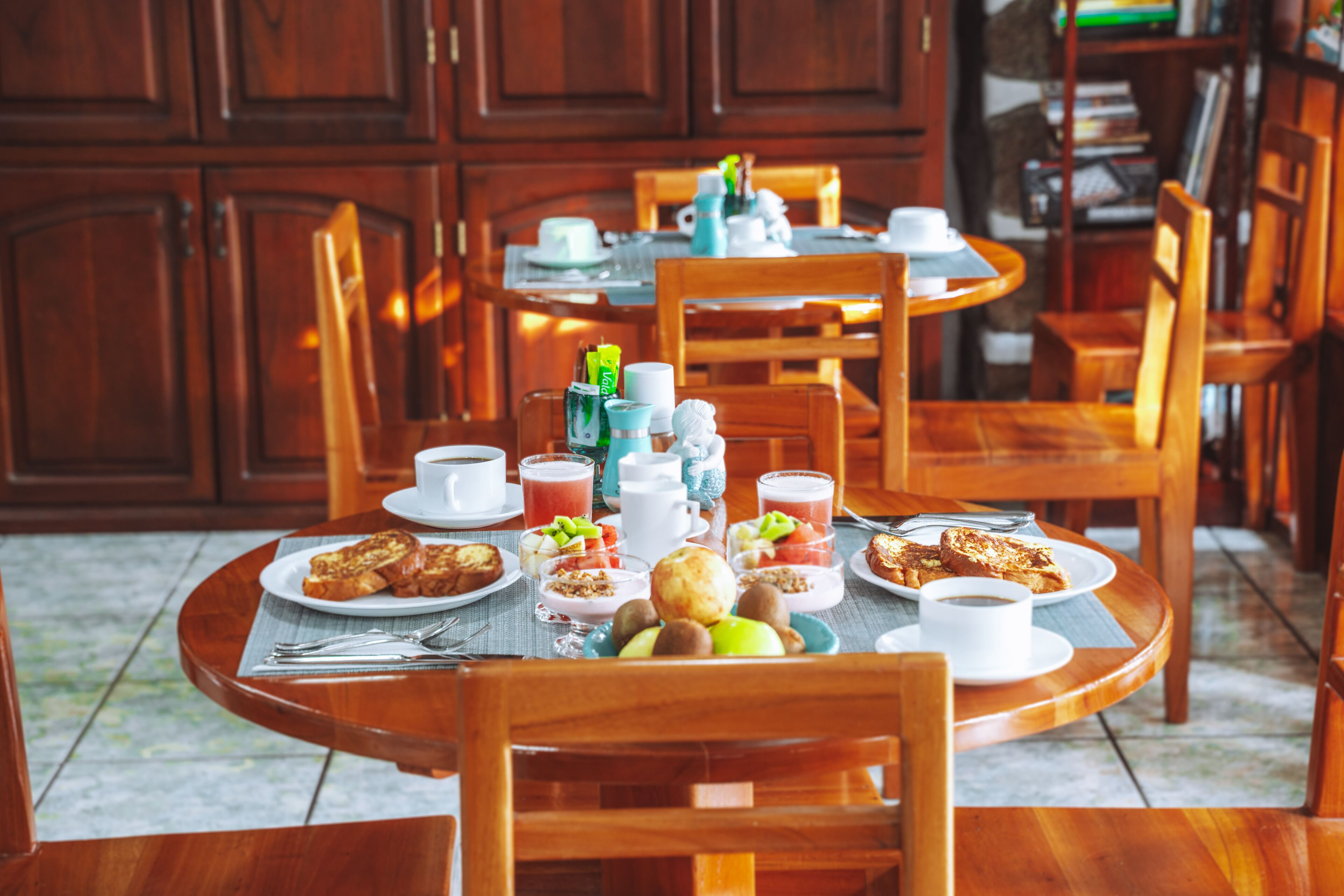 A dining area with wooden tables and chairs, breakfast items, and a coffee station.