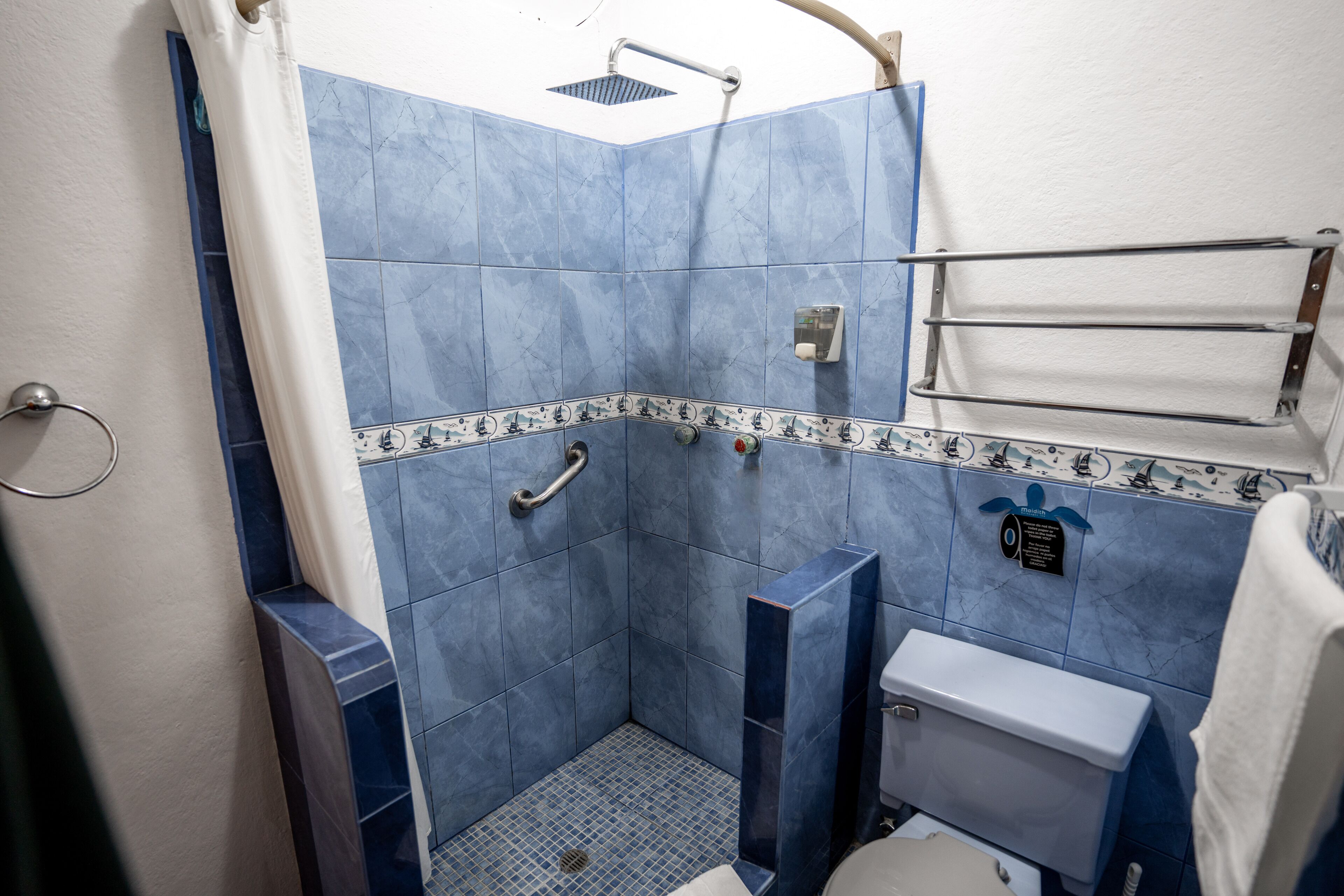 A bathroom with blue tiles, a shower, a toilet, and a towel rack.