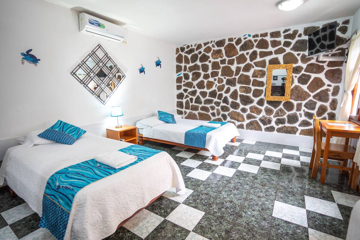 Ein Hotelzimmer mit zwei Betten, einer Steinwand, einem Schachbrettfußboden und einem kleinen Tisch.