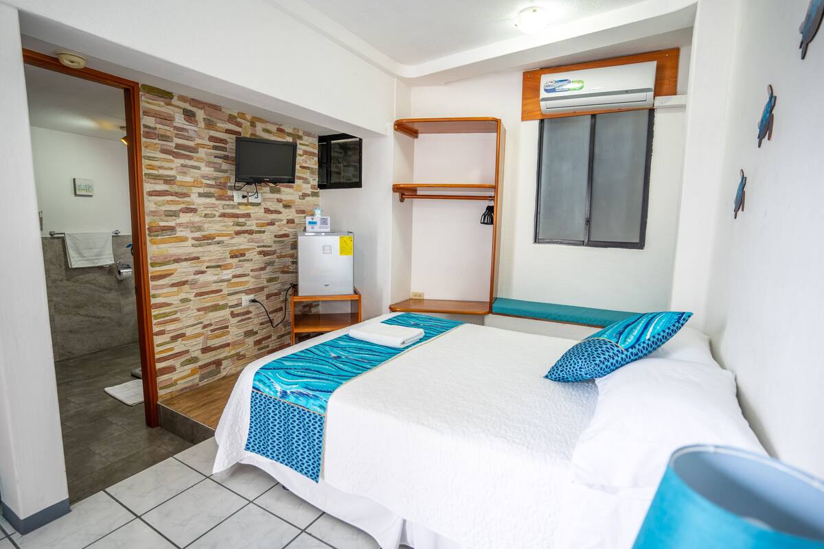 Ein Hotelzimmer mit Bett, kleinem Schreibtisch, Wand-Fernseher und Duschbereich.