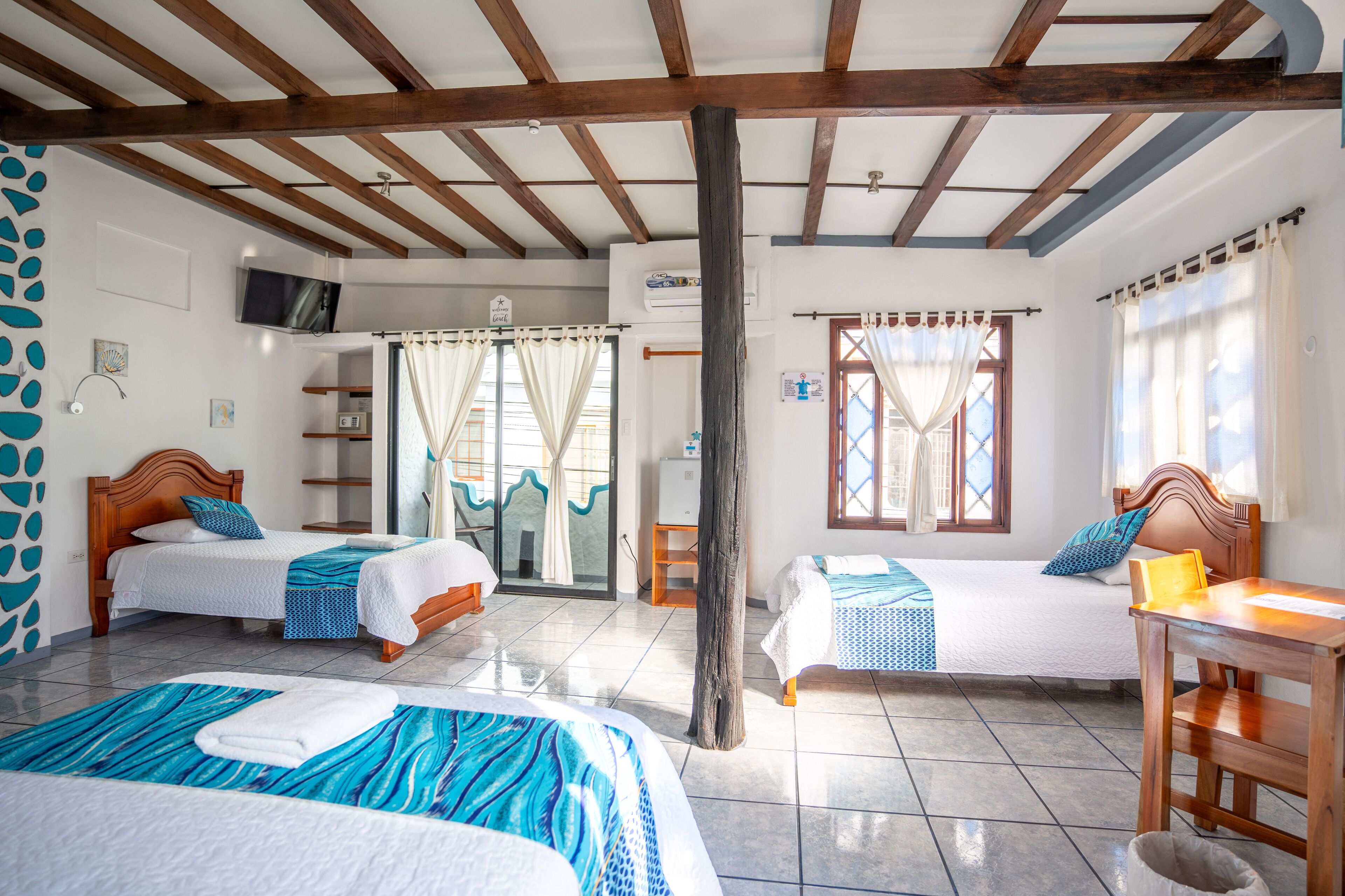 Habitación de hotel con dos camas, techo de madera, televisión y ventana con cortinas.