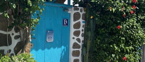 A blue gate with a sign, a mosaic-tiled entrance, and a cactus plant.