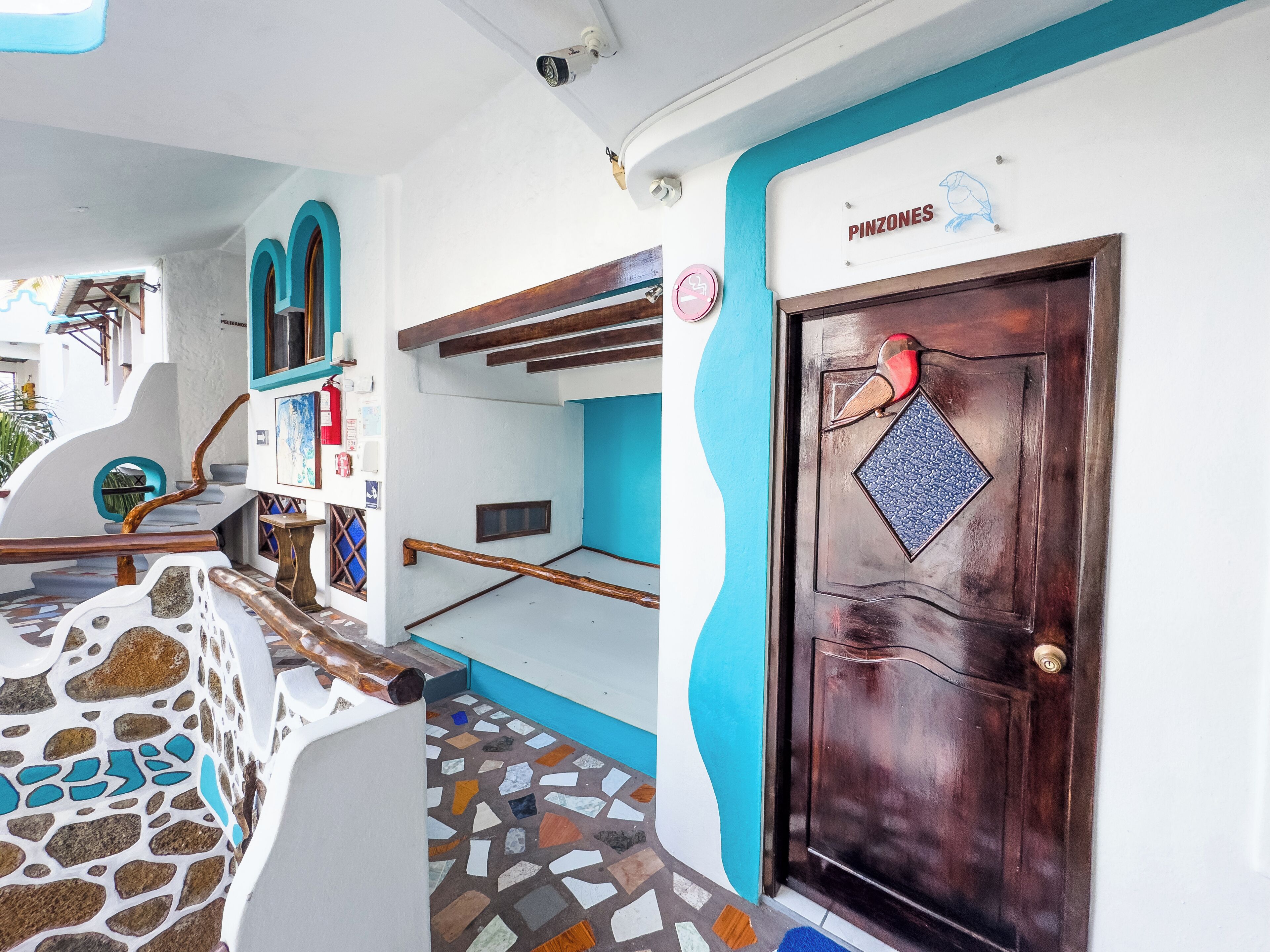 Un interior moderno con una puerta de madera que dice 'PINZONES', una escalera de diseño singular y un suelo de baldosas.