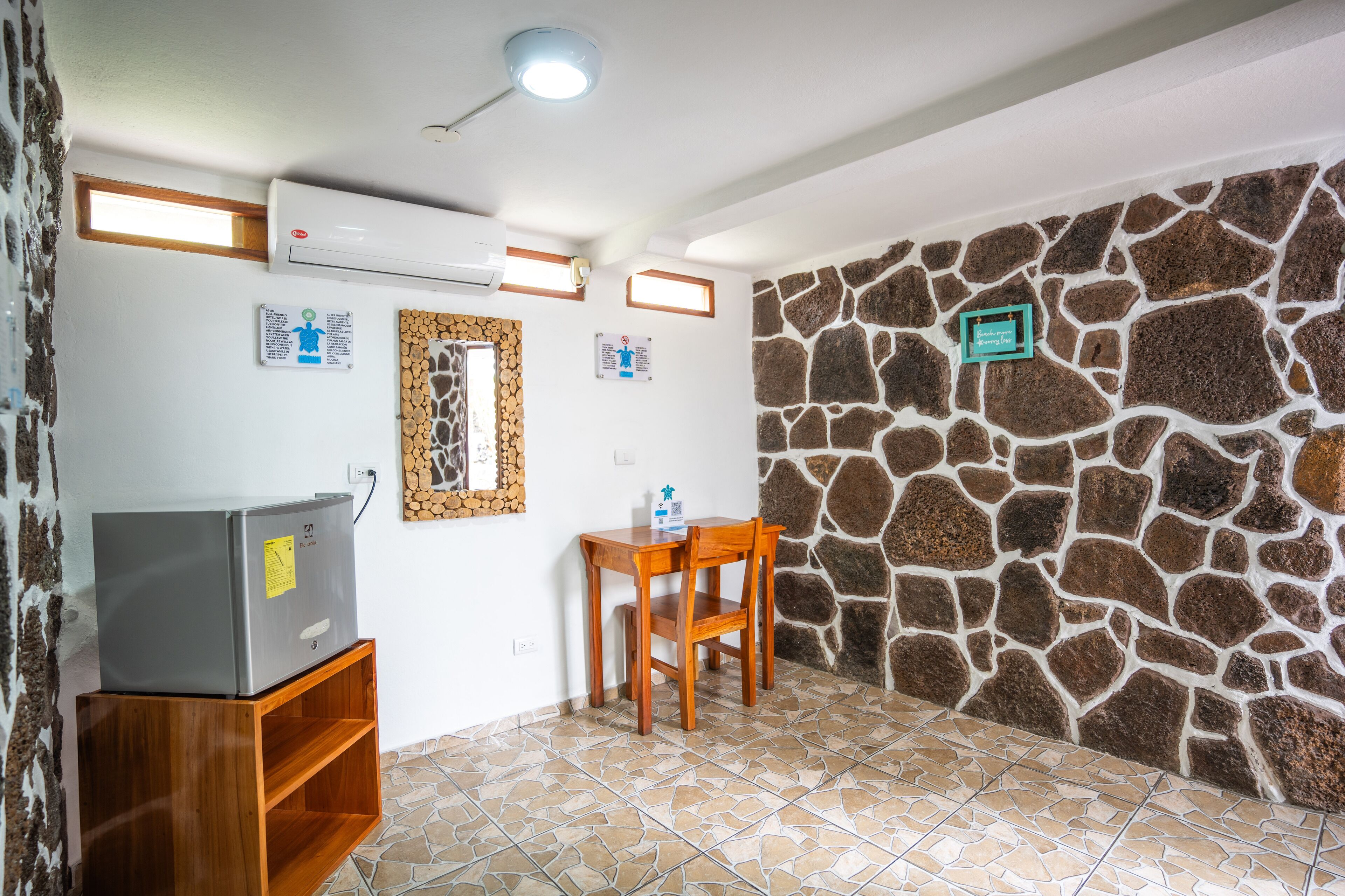 A small room with a stone wall, a wooden chair, a small table, and a refrigerator.