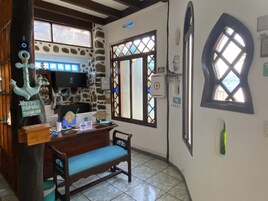 Una habitación con pared de piedra, muebles de madera, un escritorio con computadora y una ventana con marco decorativo.
